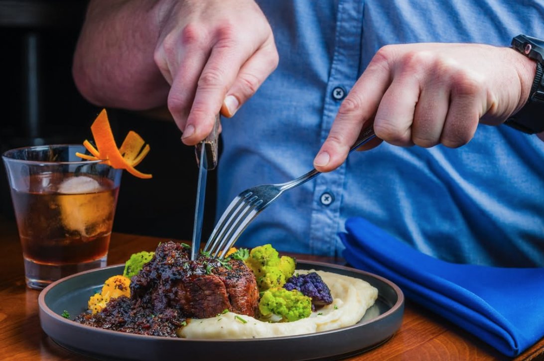 Guest enjoying a plated Oakmont dinner alongside a craft cocktail